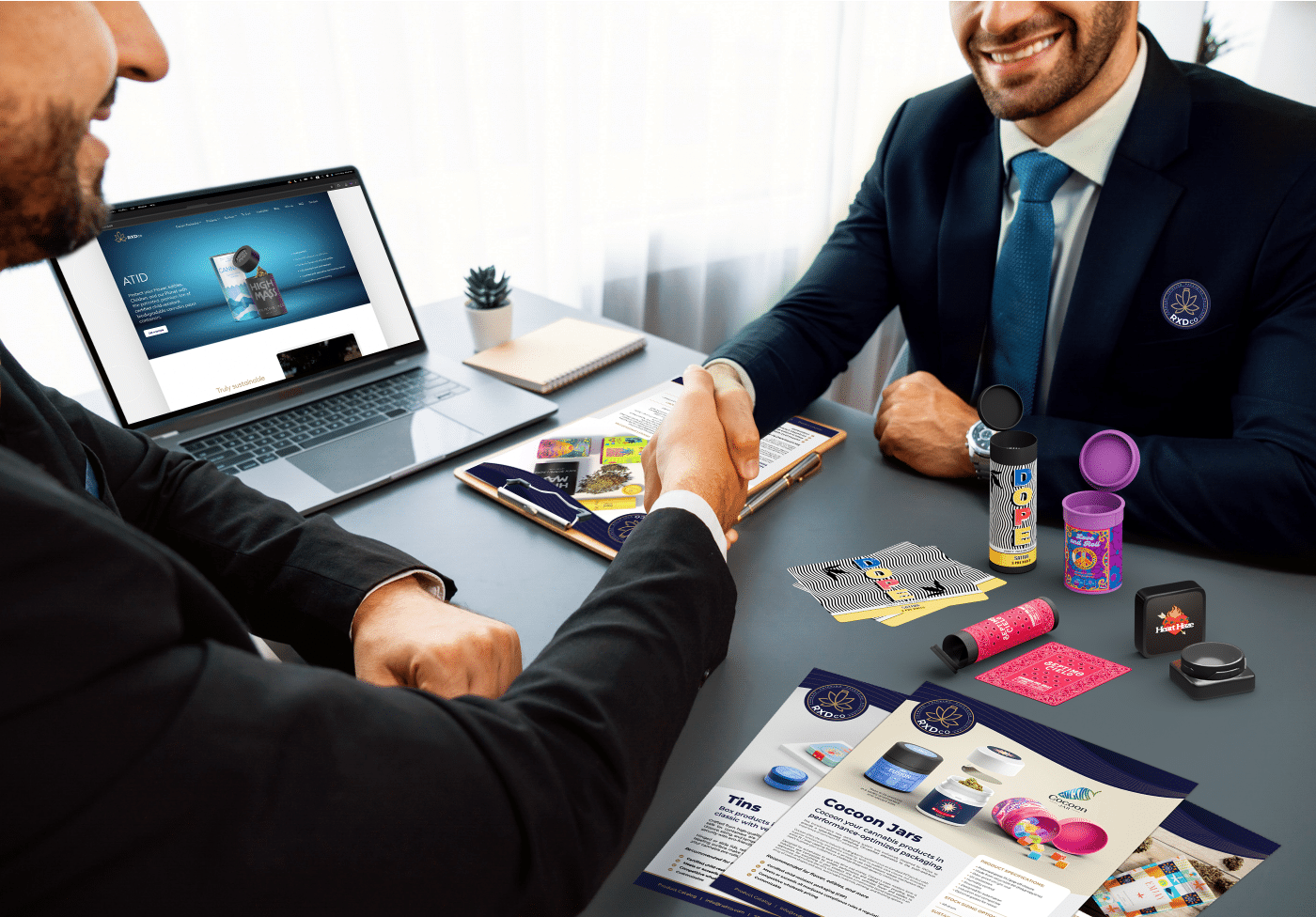 Two professionals shaking hands at a cannabis packaging meeting with RXDco sample jars, print materials, and custom label mockups on the table
